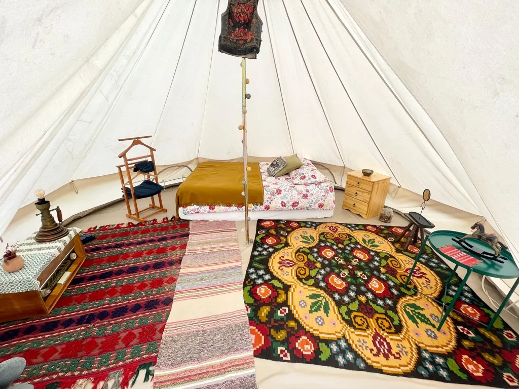 Interiorul cortului de glamping cu pat confortabil și lumină caldă
