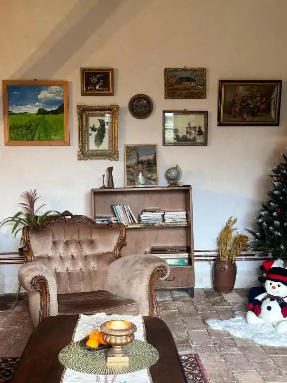 Living-room wall with framed landscape paintings, a tufted armchair and a bookshelf with old books