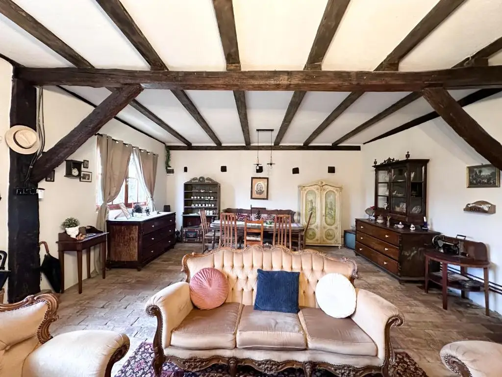 Large common living room with dark ceiling beams, a vintage sofa with cushions, antique dressers and a dining table