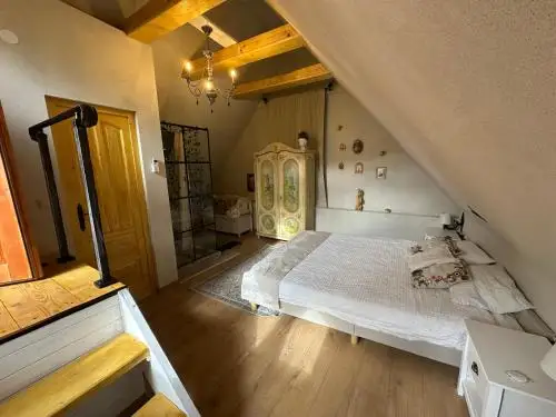 Attic bedroom with a white bed, a hand-painted wardrobe and a glass shower cabin under the eaves