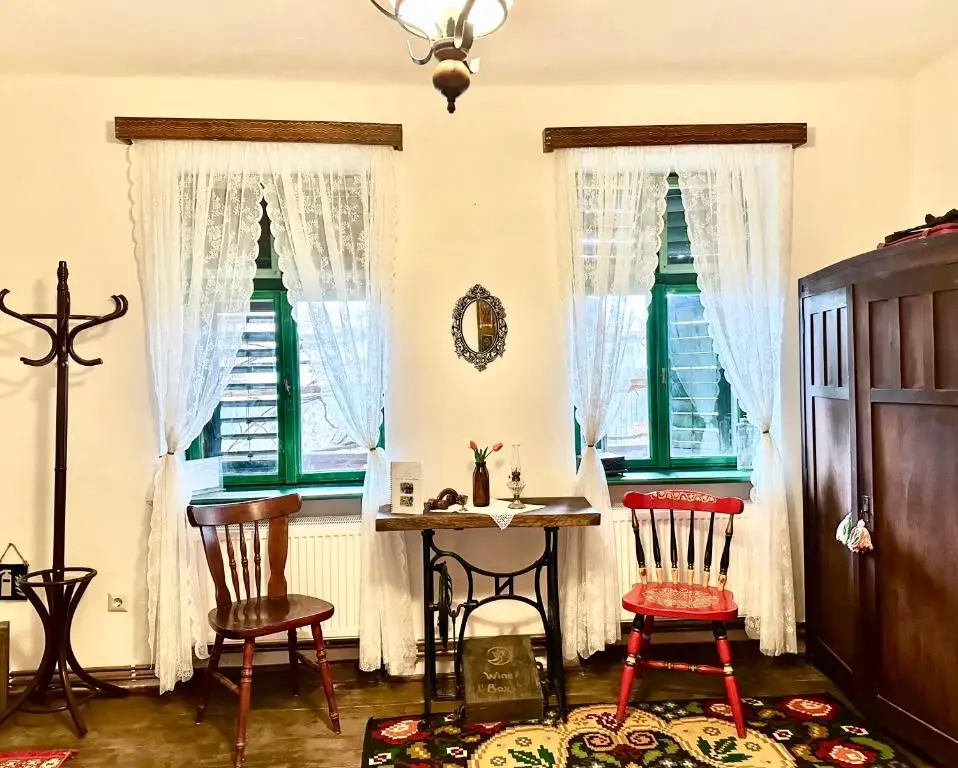 Sitting corner with an old sewing-machine table, a red folk-painted chair and windows with green frames and lace curtains