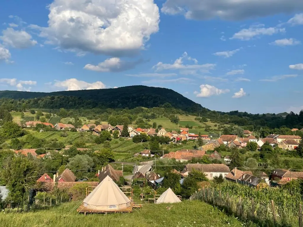 Panorama over the village of Saschiz and its rolling hills, with two white bell tents pitched in the meadow above the house